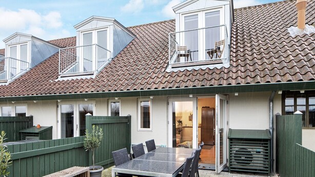 A residential building with a tiled roof, dormer windows, a balcony, and a sliding glass door entrance. - Karrebaeksminde Apartments (Karrebæksminde)