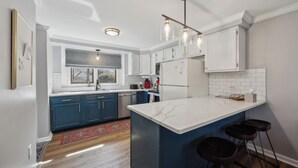 Een moderne keuken met witte kasten, een marmeren eiland en barstoelen.
