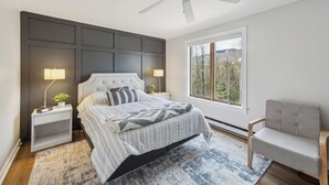 Een slaapkamer met een bed, nachtkastjes, een stoel, een plafondventilator en een raam met uitzicht.