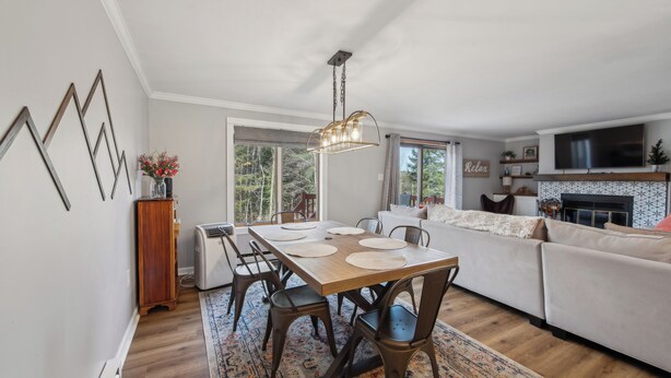 Een moderne woonkamer met een open haard, een eethoek met een houten tafel en stoelen, en een bank.