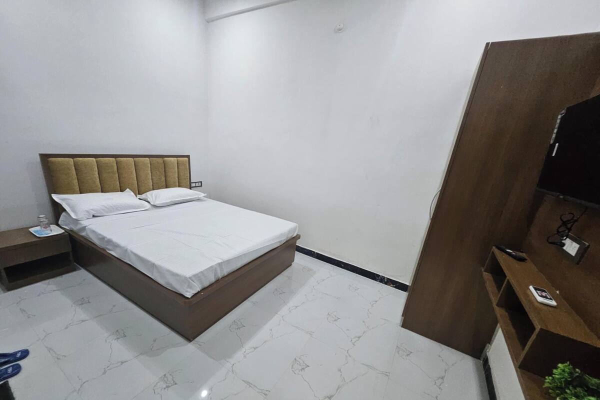 Un dormitorio con cama, mesita de noche, mueble para televisión y una planta en maceta.
