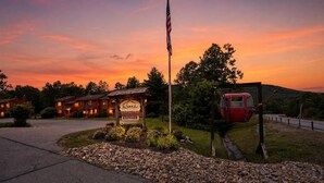 Mökki, jonka edessä on kyltti, lippu ja punainen ajoneuvo.