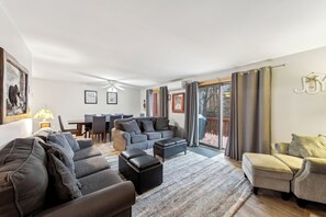 Ein modernes Wohnzimmer mit einer Sofagarnitur, einem Hocker und einem Essbereich mit Stühlen und einem Tisch.