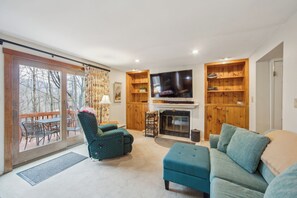 Ein Wohnzimmer mit Kamin, Fernseher und Blick ins Freie.