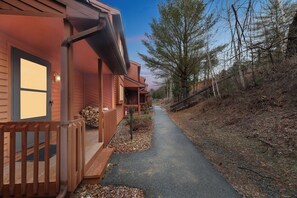 Eine Holzhütte mit Veranda, einem Weg und einem bewaldeten Hügelhang.