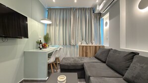 A modern living room with a flat-screen TV, a sofa, a coffee table, and a dining area with a small table and chairs. - SmartLiving Central Apt 7 (Thessaloniki)