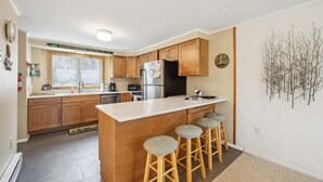 Une cuisine moderne avec des meubles en bois, un réfrigérateur en acier inoxydable et un coin bar avec des tabourets.