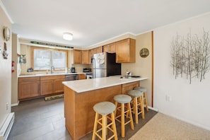A modern kitchen with wooden cabinets, a stainless steel refrigerator, and a bar stool seating area.