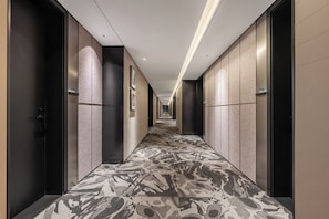 A hotel corridor with a patterned carpet, dark walls, and framed pictures on the walls.
