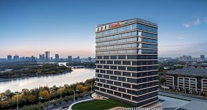 A modern hotel with a multi-story structure, large windows, and a view of a river and city skyline. - Intercity Hotel Qingdao Sino-Euro Sea (Qingdao)