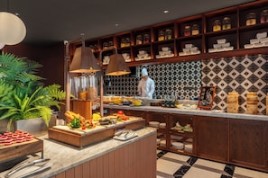 A kitchen with a chef, a buffet counter, and shelves with jars. - Intercity Hotel Qingdao Sino-Euro Sea (Qingdao)