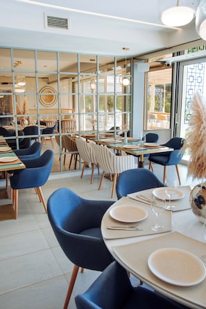 A restaurant with tables set for dining, chairs, and a view through a glass partition. - Status M Apartments 99 (Becici)
