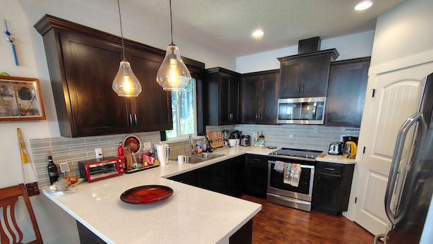 Una cocina con alacenas de madera oscura, una isla grande, electrodomésticos de acero inoxidable e iluminación colgante.