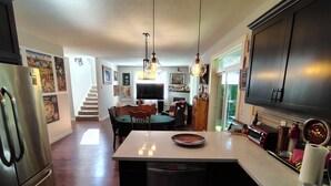 Una cocina con una isla central, un comedor con sillas y una mesa, un refrigerador y un televisor al fondo.