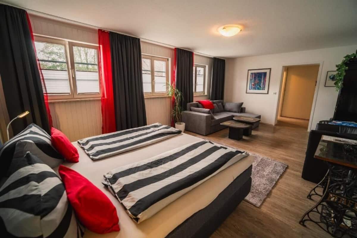 A hotel room with a bed, a sofa, a desk, and a window with curtains.
