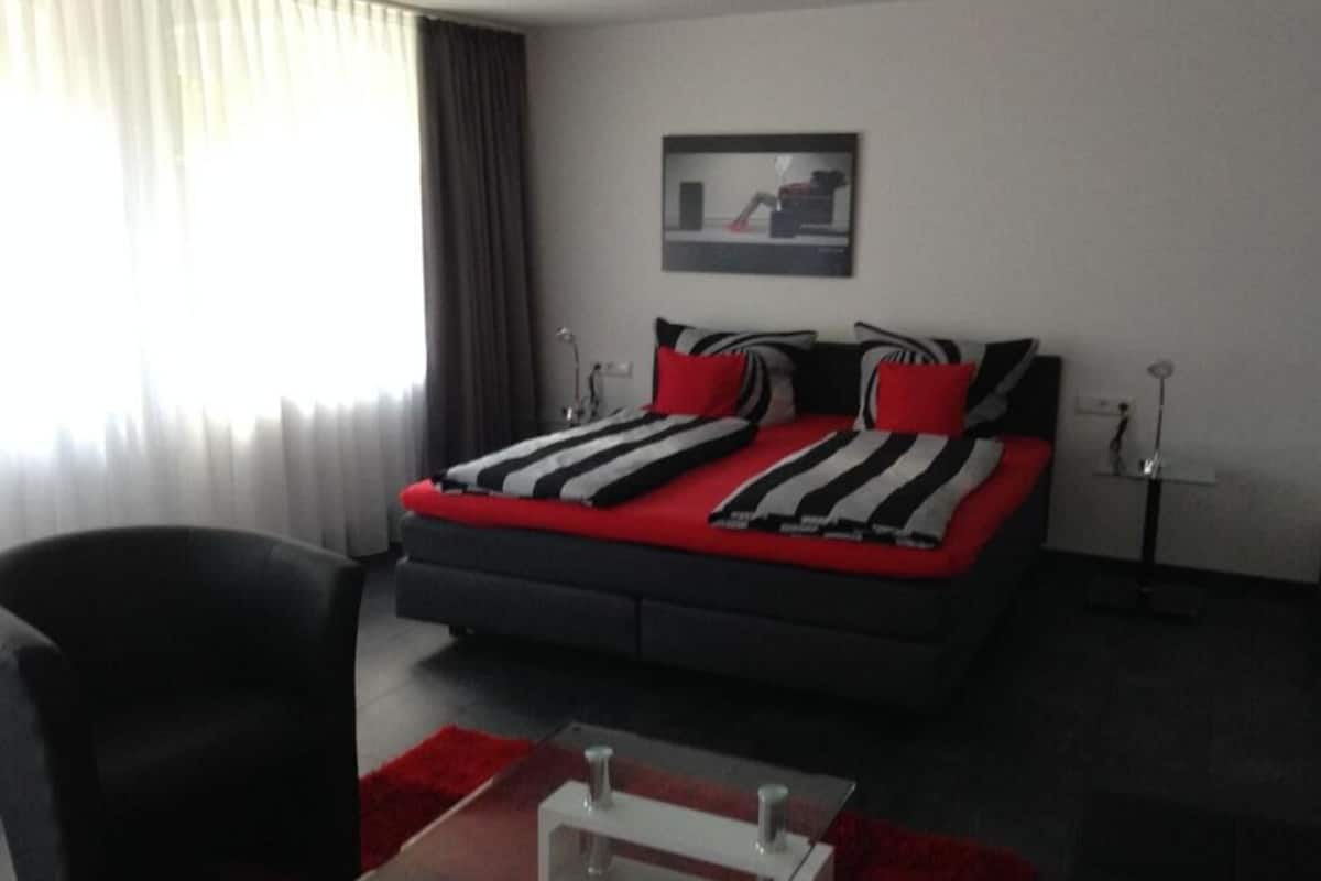 A bedroom with a bed, a chair, a desk, and a lamp.