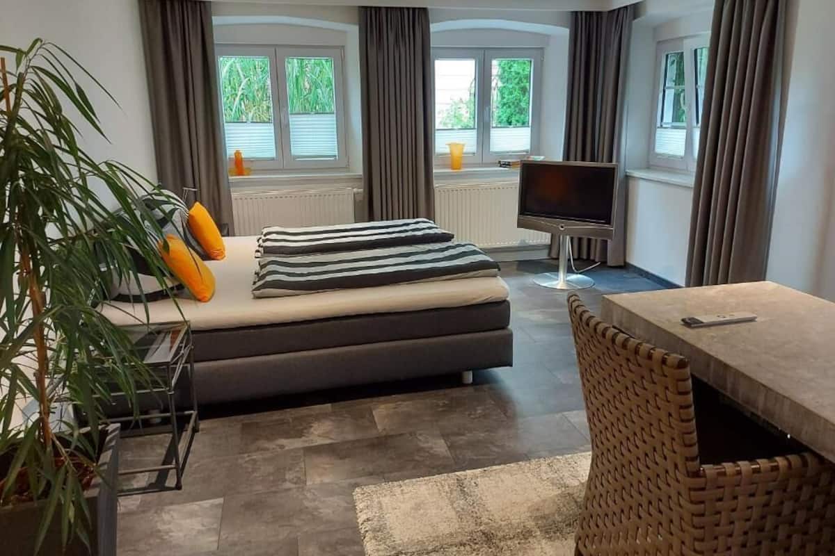 A modern hotel room with a bed, a TV, a dining table, and a large window.
