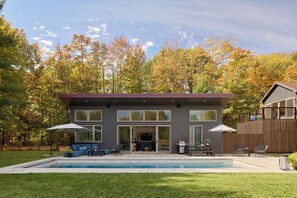 Une maison moderne dotĂ©e dâune piscine, dâun espace salon extĂ©rieur et dâune grande entrĂ©e vitrĂ©e.