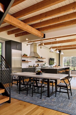 Una cocina moderna con vigas de madera, un refrigerador de acero inoxidable, una mesa de comedor con sillas y una isla grande.