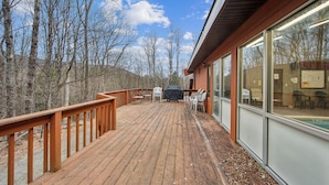 A wooden deck with outdoor seating, a barbecue grill, and a view of trees and hills. - Townhome Near Gore Mtn | Covered Heated Pool + Rec Lounge | Quick Silver (North Creek)