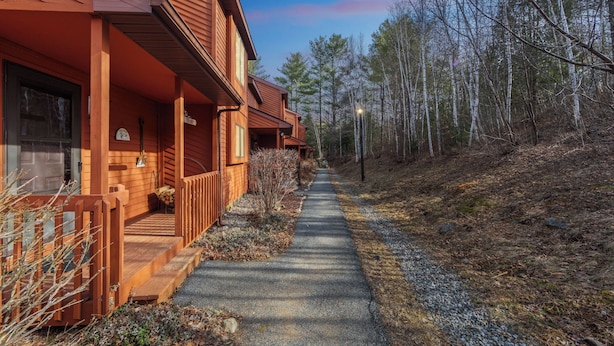 A wooden cabin with a porch, a gravel path, and a forested hillside. - Townhome Near Gore Mtn | Covered Heated Pool + Rec Lounge | Quick Silver (North Creek)