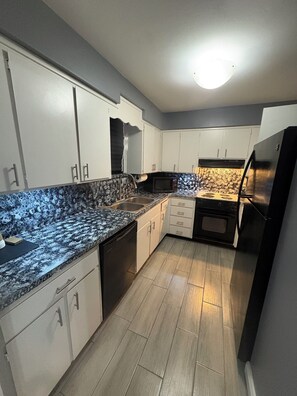 A kitchen with white cabinets, a granite countertop, a black refrigerator, and a microwave. -  2-bedroom condo by Jaguars Stadium (Jacksonville)