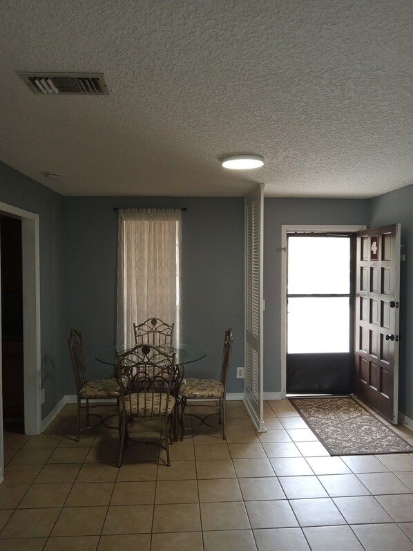 A dining area with a table and chairs, a window with curtains, a door with a number, and a tiled floor. -  2-bedroom condo by Jaguars Stadium (Jacksonville)