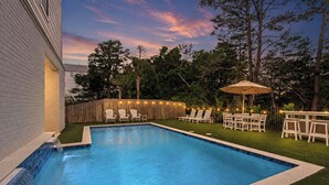 Una piscina con caída de agua, rodeada por una valla de madera y muebles de exterior.