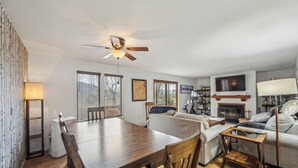 A modern living room with a dining table, sofa, TV, fireplace, and ceiling fan. - Adirondack Retreat | Covered Heated Pool + Recreation Lounge | North Side (North Creek)