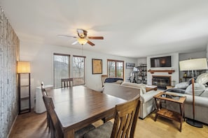 Un salon moderne comprenant une table à manger, un canapé, un téléviseur, une cheminée et un ventilateur de plafond.