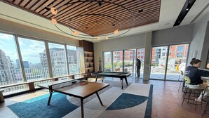 Espaço moderno em ambiente interno com mesa de bilhar, área de estar e grandes janelas com vista para a cidade.