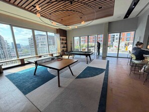 Ein moderner Innenraum mit Billardtisch, Sitzecke und großen Fenstern mit Blick auf die Stadt.