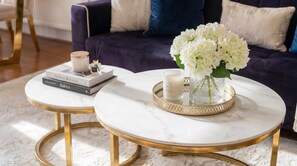Two round marble tables with gold legs, a white vase with white flowers, a candle, and a book titled 'Raloya' on a white marble surface. - MAGICAL MARBLE 3 BEDROOM KNIGHTSBRIDGE GOLDEN APARTMENT WITH BALCONY (Greater London)