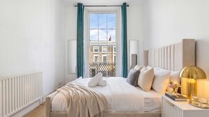 Hotelkamer met een bed, nachtkastje met lamp, raam met gordijnen en uitzicht op gebouwen.