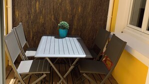 En terrasse med et bord, stole, en potteplante og en gul væg.