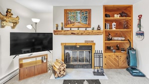 Een woonkamer met een televisie, open haard, houten planken en een schilderij.
