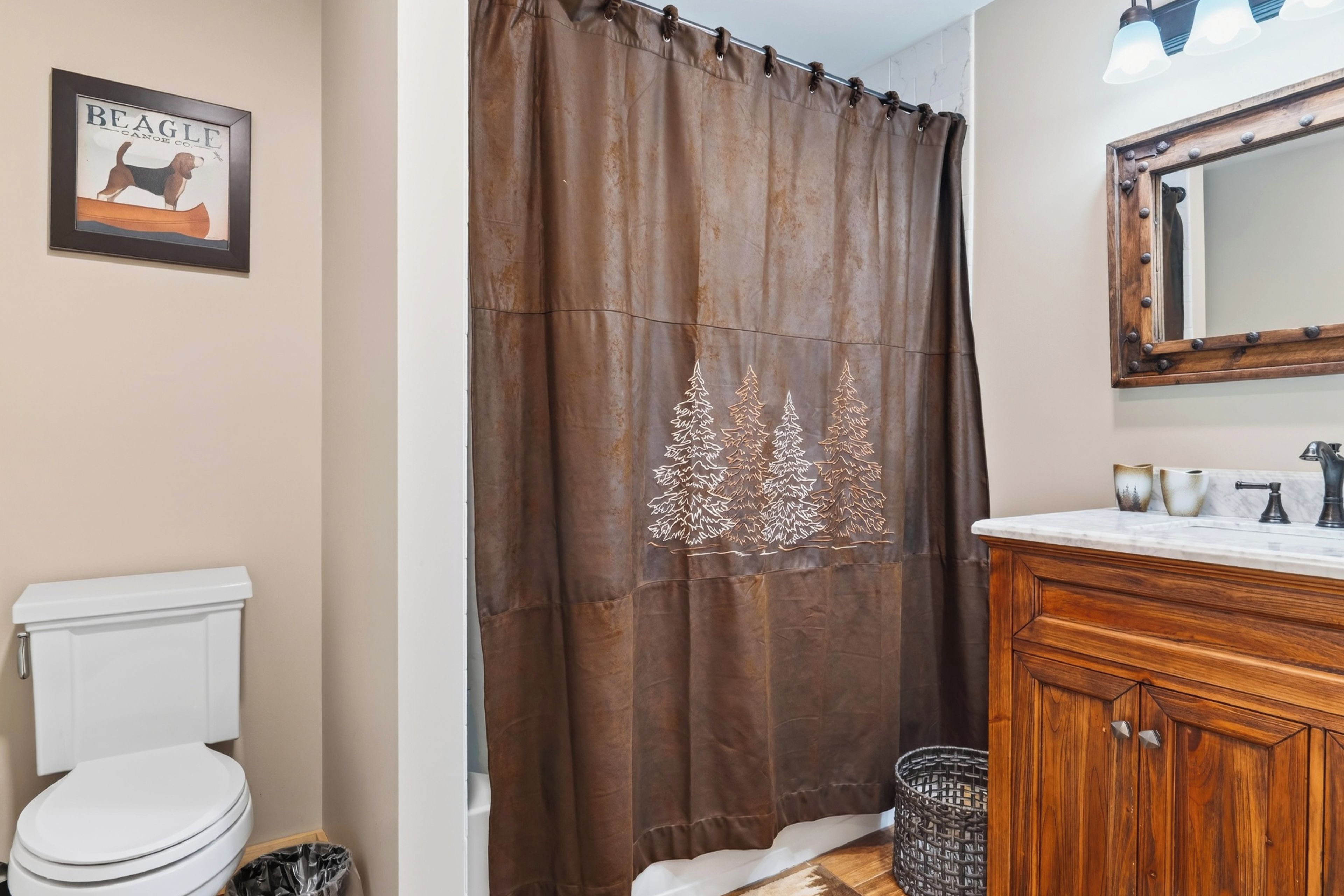 Une salle de bain comprenant des toilettes, un meuble en bois, un miroir et un rideau de douche orné d’un motif d’arbre.