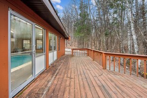 Eine Holzterrasse mit Glastüren, die zu einem Pool führen, umgeben von Bäumen.