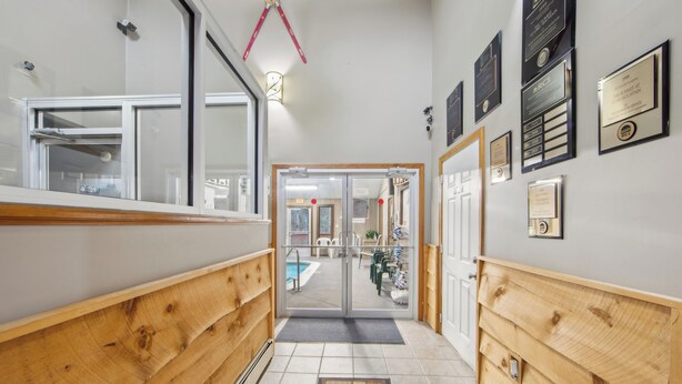 Un corridoio con rivestimenti in legno, una porta vetrata che dà su un’area piscina e diverse targhe appese alle pareti.