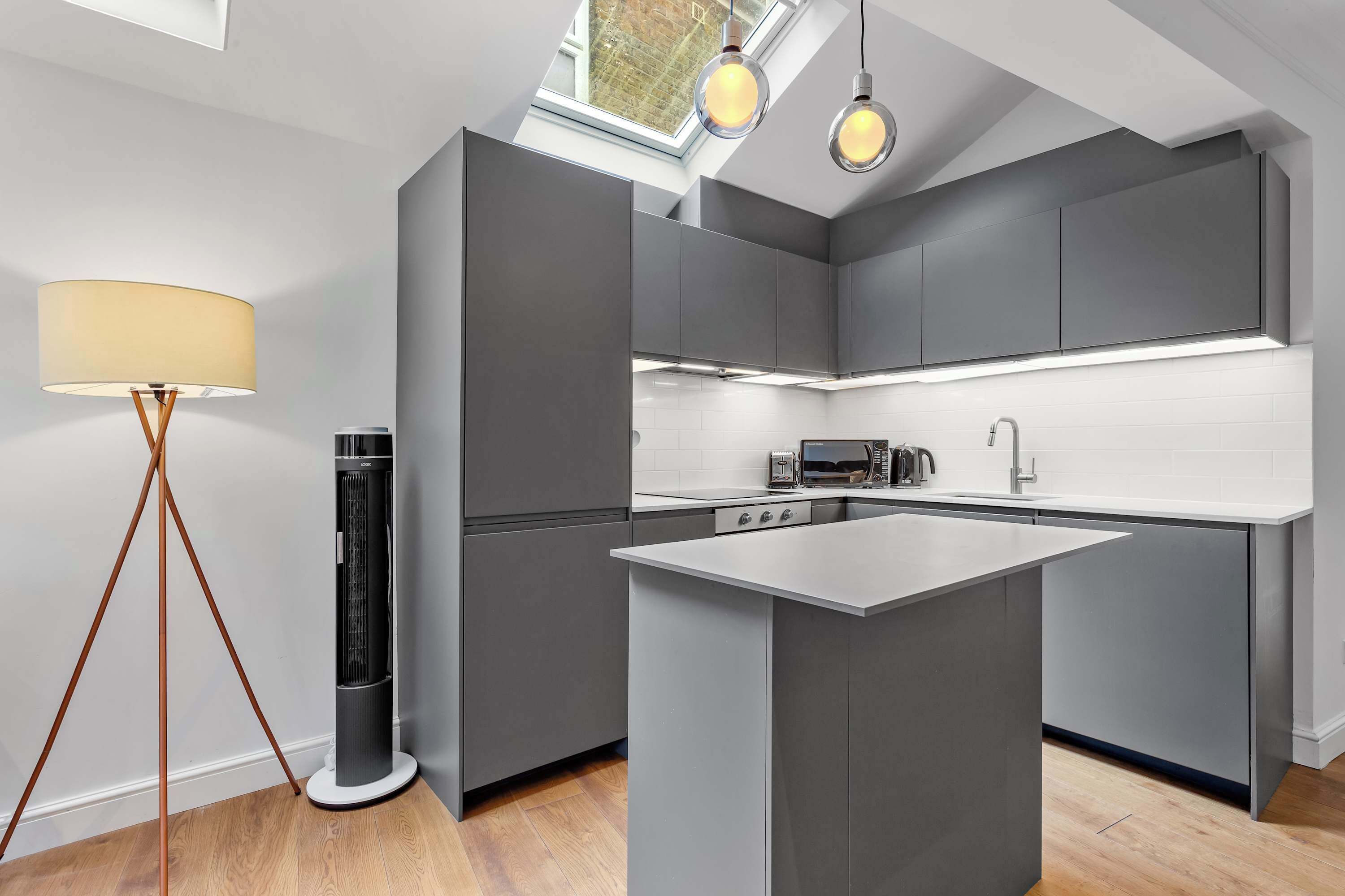 Une cuisine moderne avec des meubles de couleur grise, un îlot central et des luminaires suspendus.