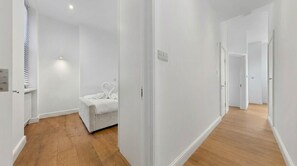 A hallway with wooden flooring, white walls, and a bed with white bedding. - VOLCANIC HOT TUB EXPERIENCE Central London 2BR Lagoon, Memories Await for 6 (Greater London)