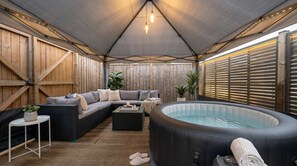 Ett takförsett utomhusområde med ett bubbelbad, sittplatser och ett bord.