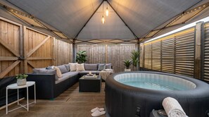 A covered outdoor area with a hot tub, seating, and a table. - VOLCANIC HOT TUB EXPERIENCE Central London 2BR Lagoon, Memories Await for 6 (Greater London)
