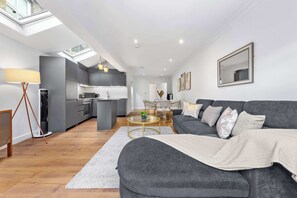 A modern living space with a grey sofa, a coffee table, and a kitchen in the background. - VOLCANIC HOT TUB EXPERIENCE Central London 2BR Lagoon, Memories Await for 6 (Greater London)