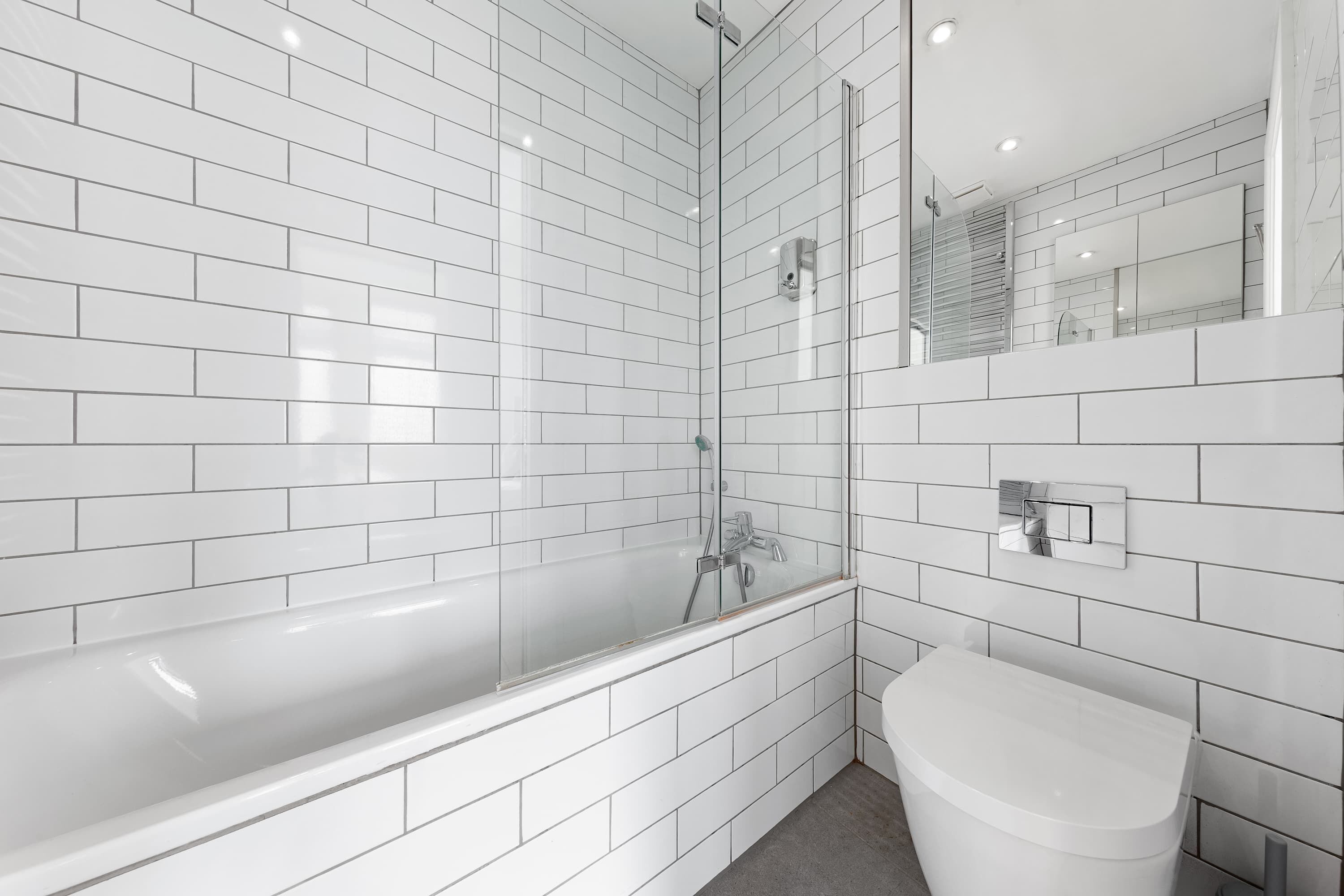 Ein Badezimmer mit weißen Fliesen im U-Bahn-Stil, einer Duschkabine, einer weißen Badewanne und einem weißen WC.