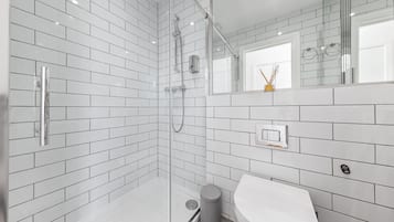 Une salle de bain moderne avec des carreaux de céramique blancs rectangulaires, une douche en verre, un lavabo blanc et un miroir agrémenté d’un petit objet décoratif fixé au mur.