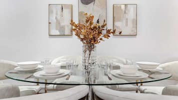 A dining table with a glass top surrounded by white chairs, set with white plates, bowls, and cutlery.