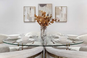 A dining table with a glass top surrounded by white chairs, set with white plates, bowls, and cutlery. - VOLCANIC HOT TUB EXPERIENCE Central London 2BR Lagoon, Memories Await for 6 (Greater London)