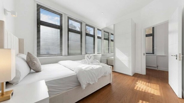A modern bedroom with a large bed, white bedding, and a view through floor-to-ceiling windows. - VOLCANIC HOT TUB EXPERIENCE Central London 2BR Lagoon, Memories Await for 6 (Greater London)
