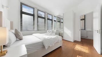 Une chambre à coucher moderne avec un grand lit, du linge de lit blanc et une vue dégagée grâce à de grandes fenêtres du sol au plafond.